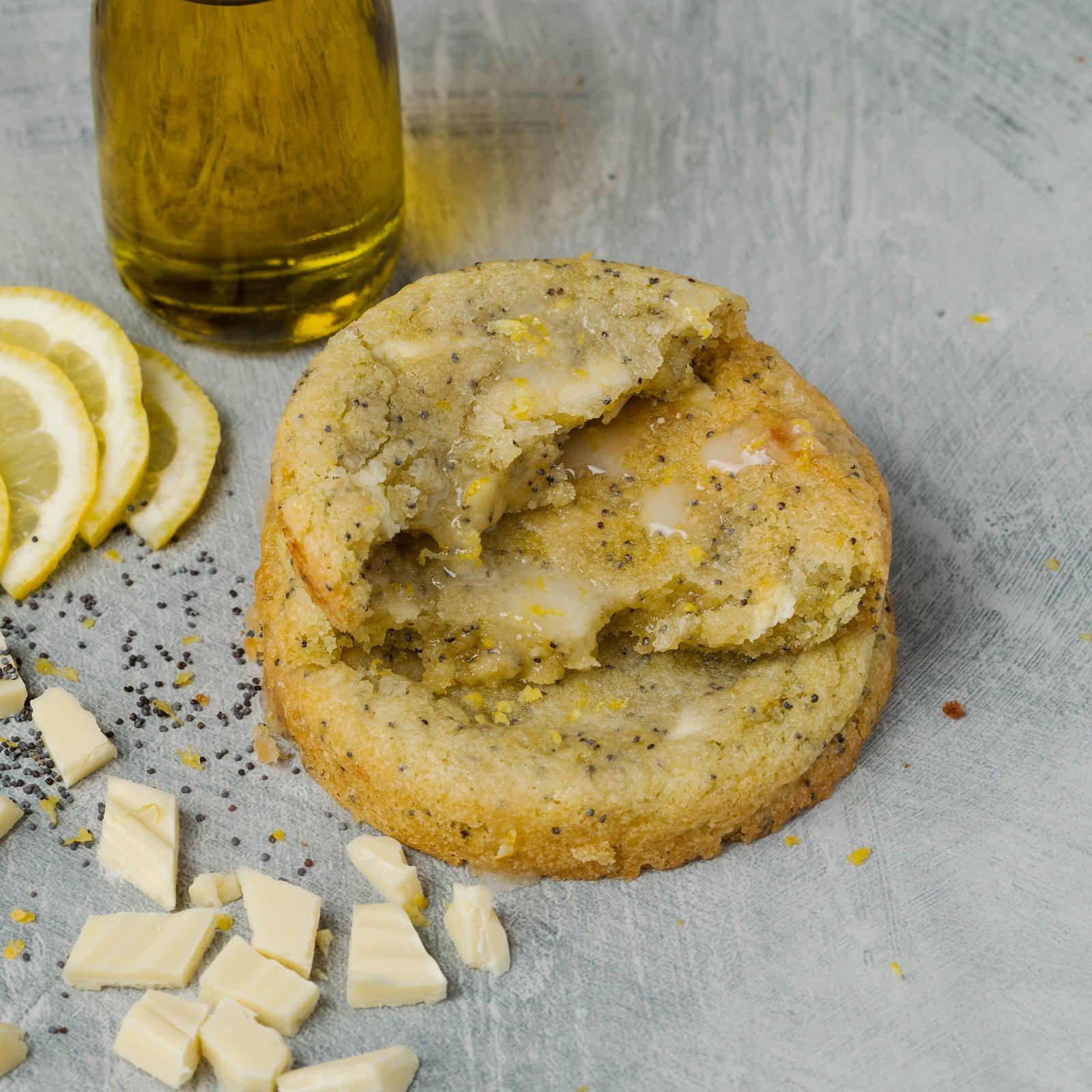 Lemon and poppy seed cookie with white glaze, broken open and styled with lemon slices, poppy seeds and white chocolate, food photography for an artisan cookie brand in Croydon.