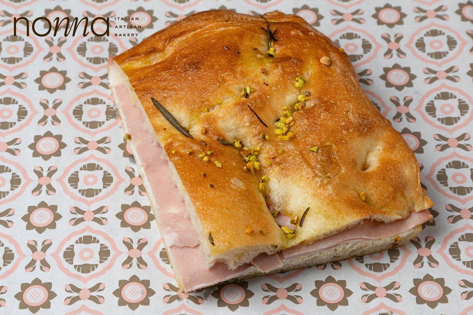 Mortadella and stracciatella focaccia cut through to show the filling, topped with chopped pistachio and rosemary, product photography for a Sicilian bakery in Holborn, London.
