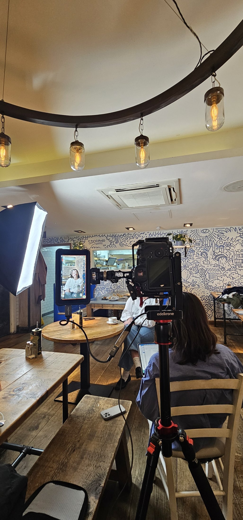 A filmed interview in progress at The Real Greek in Soho, the subject framed on the field monitor with a client-side colleague watching, restaurant video production in London.