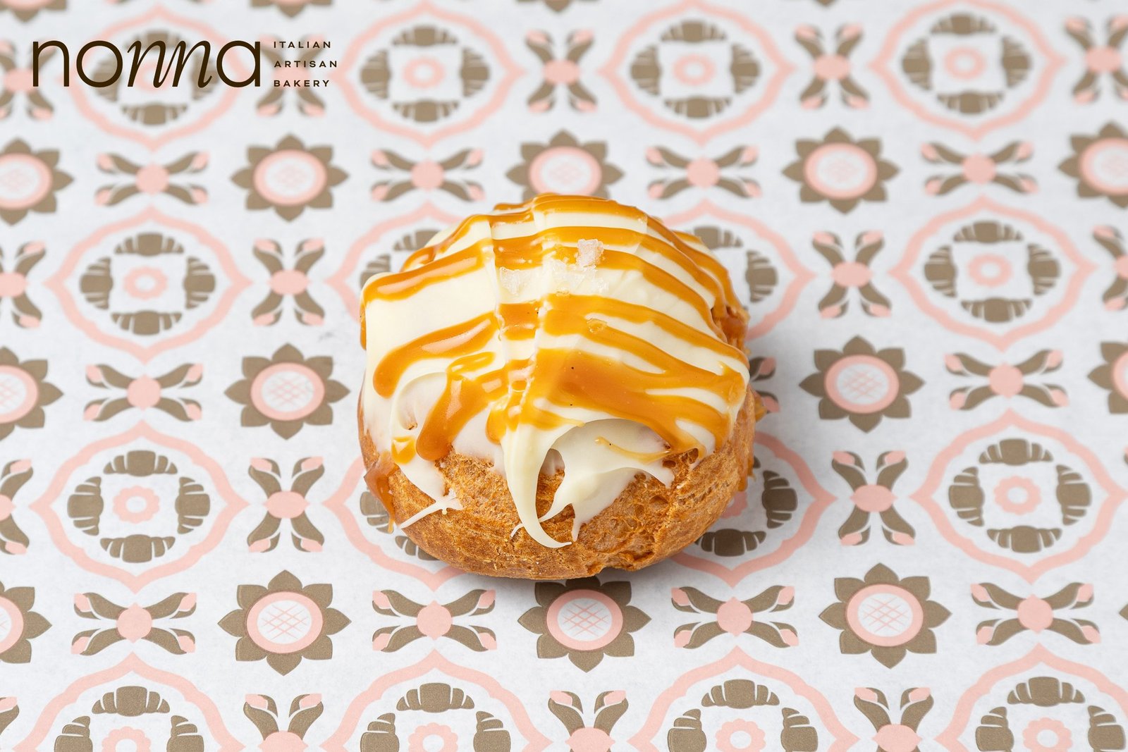 Sea salt caramel bignè, a choux bun filled with cream and drizzled with caramel, shot overhead on patterned paper, product photography for a Sicilian bakery in Holborn, London.